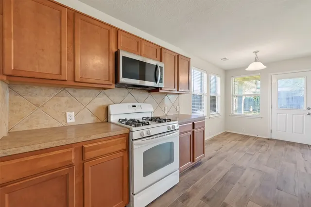 a kitchen with stainless steel appliances granite countertop a stove top oven a sink dishwasher and a refrigerator with wooden floor