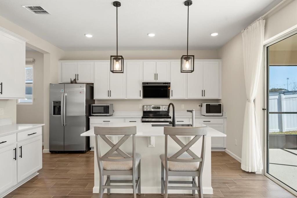 3657 Sublett Loop Tavares, FL 32778 - Photo 10 of 39 a kitchen with refrigerator a microwave a stove and white cabinets with wooden floor