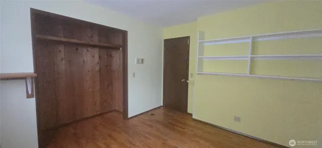 a view of an empty room with wooden floor and closet