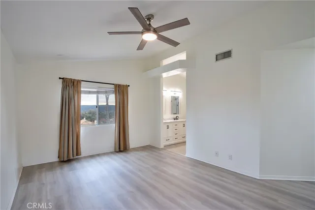 an empty room with wooden floor chandelier fan and windows