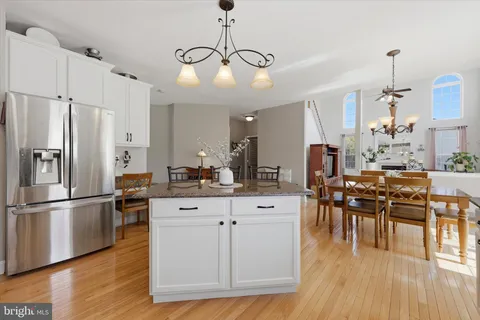 a kitchen with stainless steel appliances kitchen island granite countertop a refrigerator a stove a dining table and chairs with wooden floor
