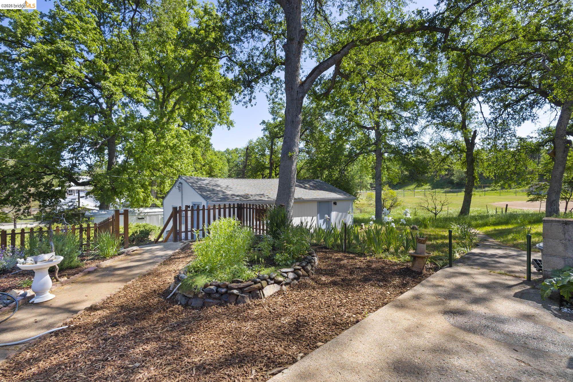18363 Yosemite Road Tuolumne, CA 95379 - Photo 19 of 34 Expansive outdoor area featuring mature trees, a detached shed with a gabled roof, and a wooden picket fence