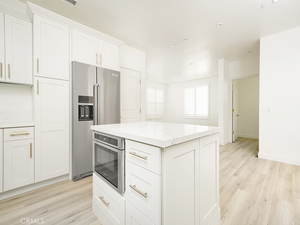 120 Messenger Irvine, CA 92618 - Photo 5 of 26 a kitchen with stainless steel appliances a stove a refrigerator and white cabinets with wooden floor