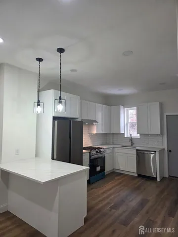 a kitchen with stainless steel appliances kitchen island granite countertop a refrigerator a stove top oven a sink and dishwasher with wooden floor