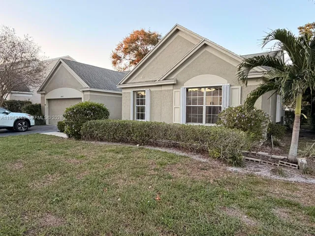 a view of a white house next to a yard with potted plants