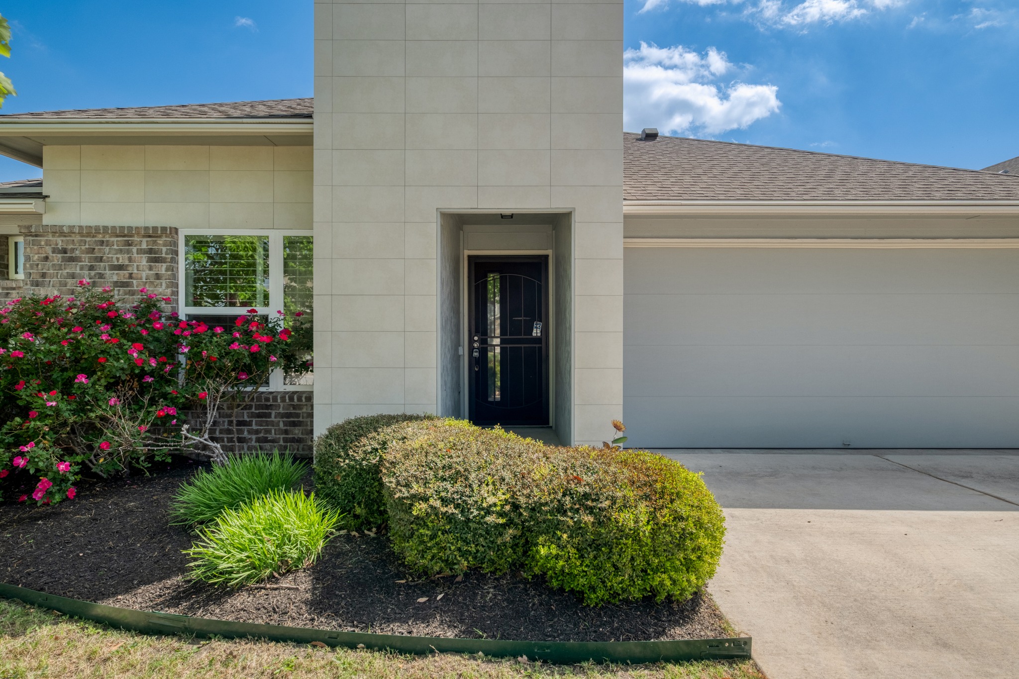 Property entrance with a shingled roof, concrete driveway, an attached garage, and brick siding