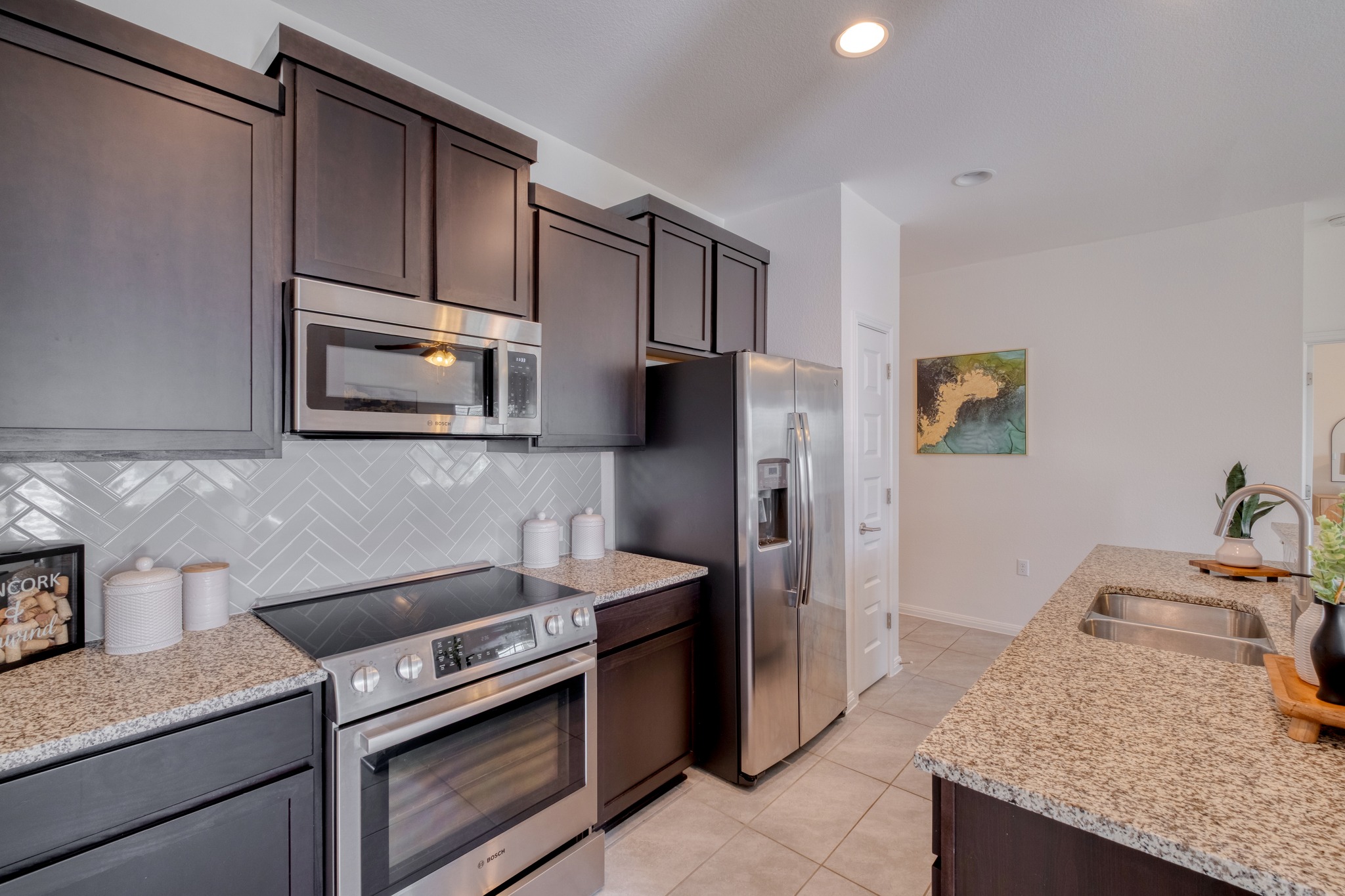 16400 Fetching Avenue Manor, TX 78653 - Photo 12 of 32 Kitchen with stainless steel appliances, dark wood finish cabinetry, light stone counters, light tile patterned floors, and recessed lighting