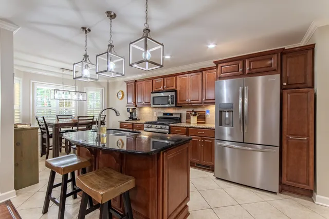 a kitchen with stainless steel appliances granite countertop a refrigerator a sink dishwasher a dining table and chairs with wooden floor