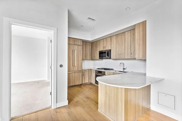 a kitchen with stainless steel appliances granite countertop a refrigerator a sink a stove a microwave and white cabinets with wooden floor