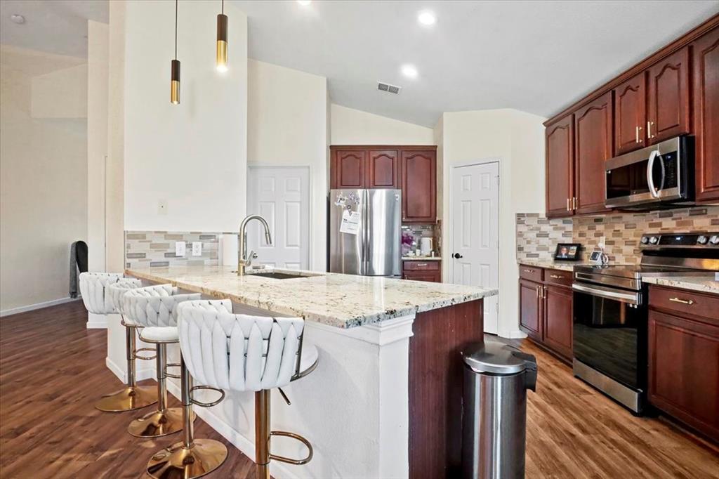 1412 Cheyenne Road Wylie, TX 75098 - Photo 10 of 24 a kitchen with stainless steel appliances kitchen island granite countertop a table chairs in it and wooden floors