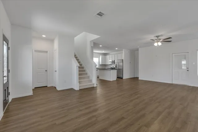 a view of an empty room with wooden floor and a kitchen