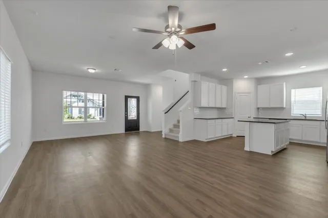 an empty room with wooden floor ceiling fan and windows