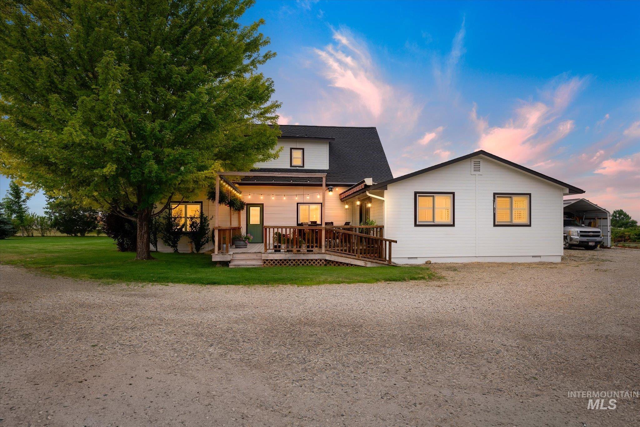 1140 Edgemont Road Emmett, ID 83617 - Photo 50 of 50 White exterior with black trim, a spacious wooden deck with string lighting, a substantial green tree, a manicured lawn, and a graveled drive