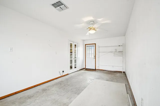 an empty room with windows and chandelier fan