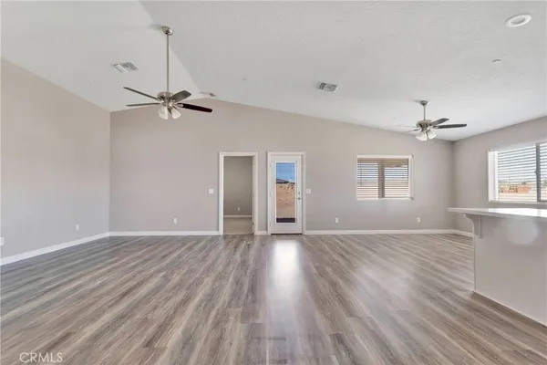 a view of an empty room with wooden floor and a ceiling fan