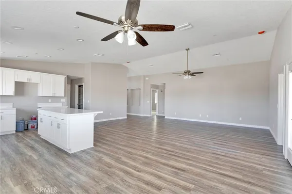 an empty room with wooden floor a ceiling fan and kitchen view
