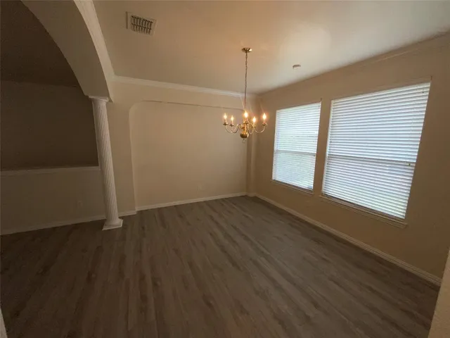 an empty room with wooden floor chandelier and windows