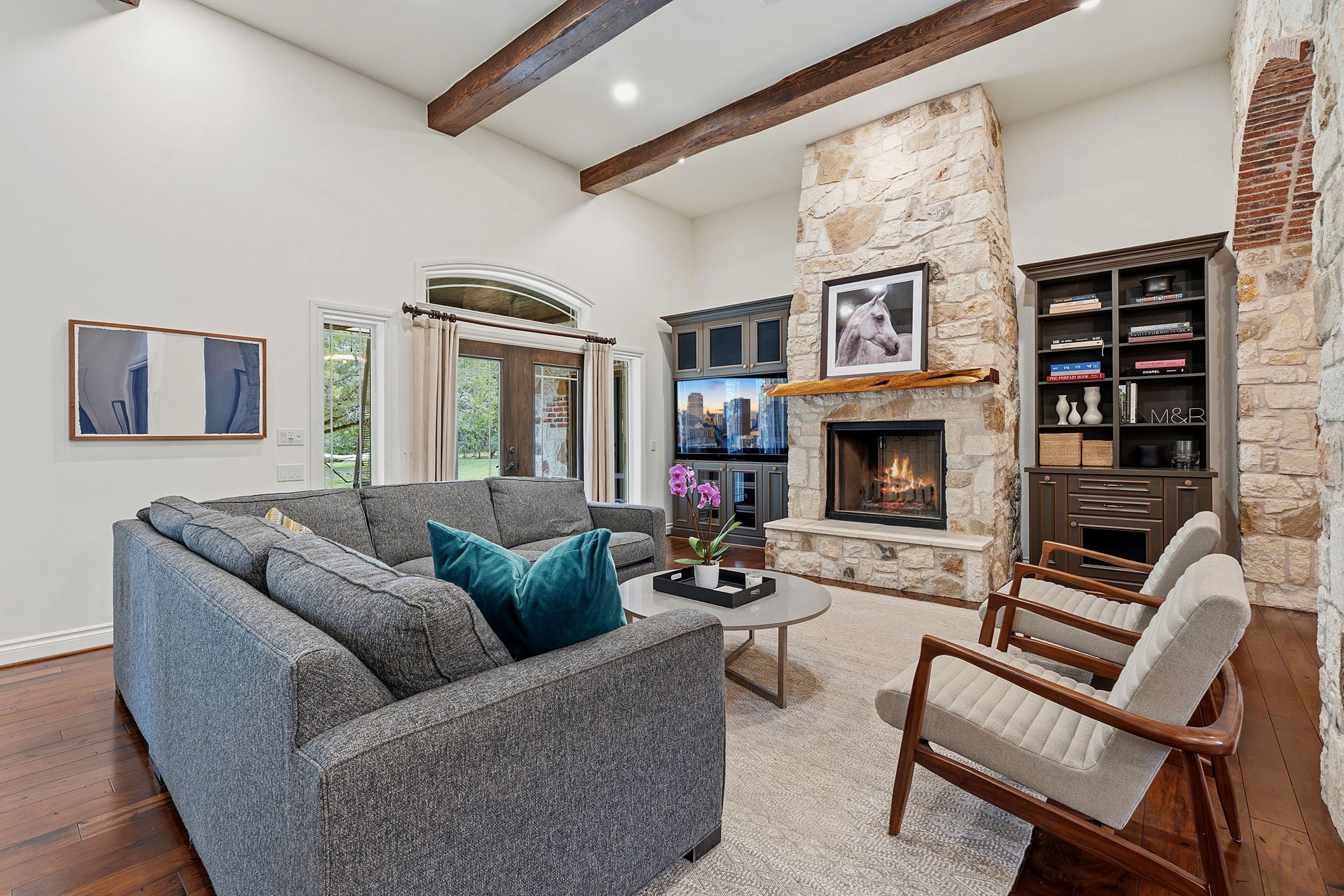 8121 Bluff Trail Austin, TX 78737 - Photo 12 of 40 A spacious living area with hardwood floors, a stone fireplace, and rustic exposed beams offers elegant comfort.