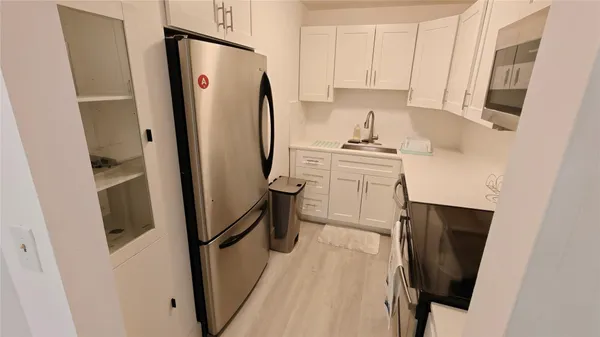 a kitchen with stainless steel appliances a refrigerator a sink a stove a washer dryer and white cabinets