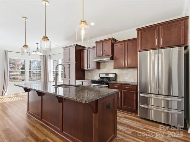 a kitchen with stainless steel appliances granite countertop a refrigerator a sink dishwasher a stove and a refrigerator with wooden floor