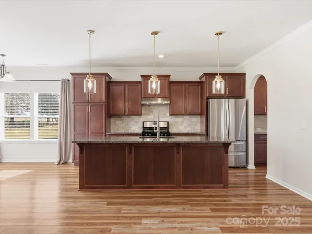 a kitchen with stainless steel appliances granite countertop a refrigerator a sink dishwasher a stove and a wooden floor