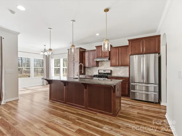 a kitchen with stainless steel appliances granite countertop a refrigerator a stove a sink dishwasher a oven and a dining table with wooden floor