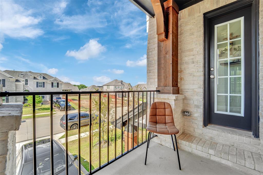 3520 Helios Lane Corinth, TX 76208 - Photo 29 of 37 Balcony featuring light-colored brick, a black iron railing, a dark entry door with glass panels, a concrete floor, and an exposed wood beam detail