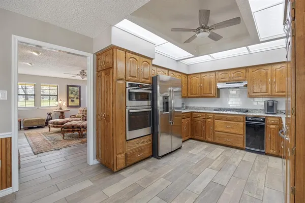 a large kitchen with stainless steel appliances granite countertop a refrigerator a sink dishwasher a stove and white countertops with wooden floor