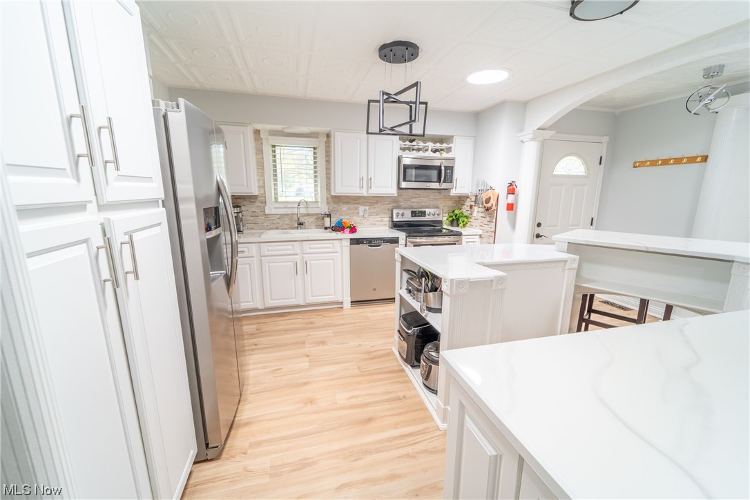 44790 Middle Ridge Road Amherst, OH 44001 - Photo 10 of 23 Kitchen with backsplash, light countertops, a kitchen island, white cabinetry, appliances with stainless steel finishes, and light hardwood flooring