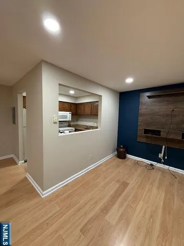 a view of an empty room with wooden floor and a kitchen