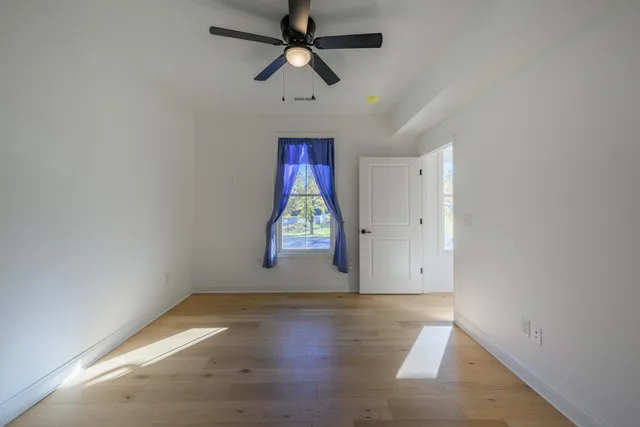 an empty room with wooden floor ceiling fan and windows
