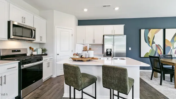 a kitchen with stainless steel appliances granite countertop a stove a sink a microwave a refrigerator and white cabinets with wooden floor