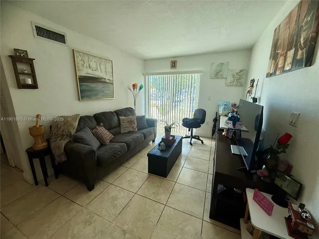 a living room with furniture potted plant floor to ceiling window and a flat screen tv