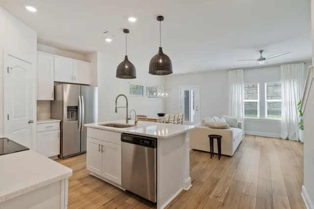 a living room with stainless steel appliances kitchen island a table chairs in it and wooden floors