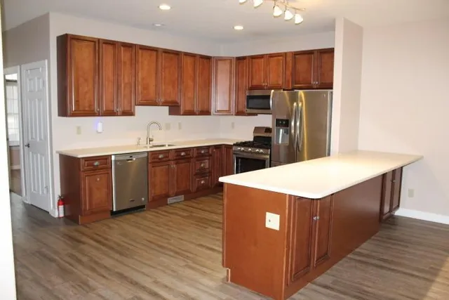 a kitchen with stainless steel appliances a sink a stove a refrigerator cabinets and wooden floor