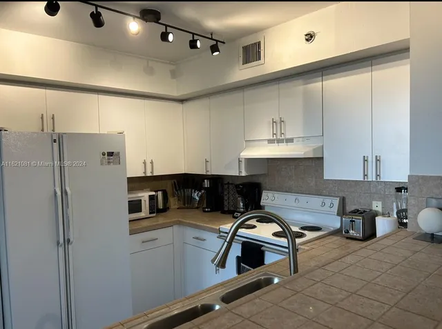 a kitchen with stainless steel appliances granite countertop a refrigerator a sink and white cabinets
