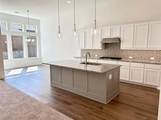 a kitchen with stainless steel appliances granite countertop a sink a stove and white cabinets with wooden floor