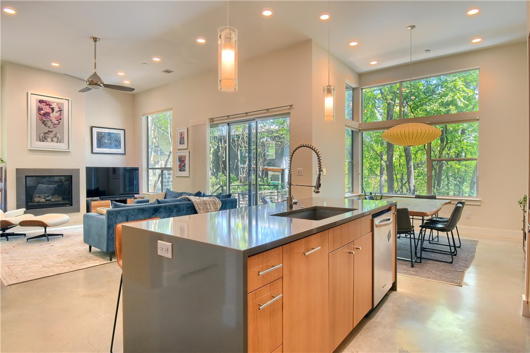 a view of a kitchen with kitchen island a large window cabinets a sink a stove and a dining table