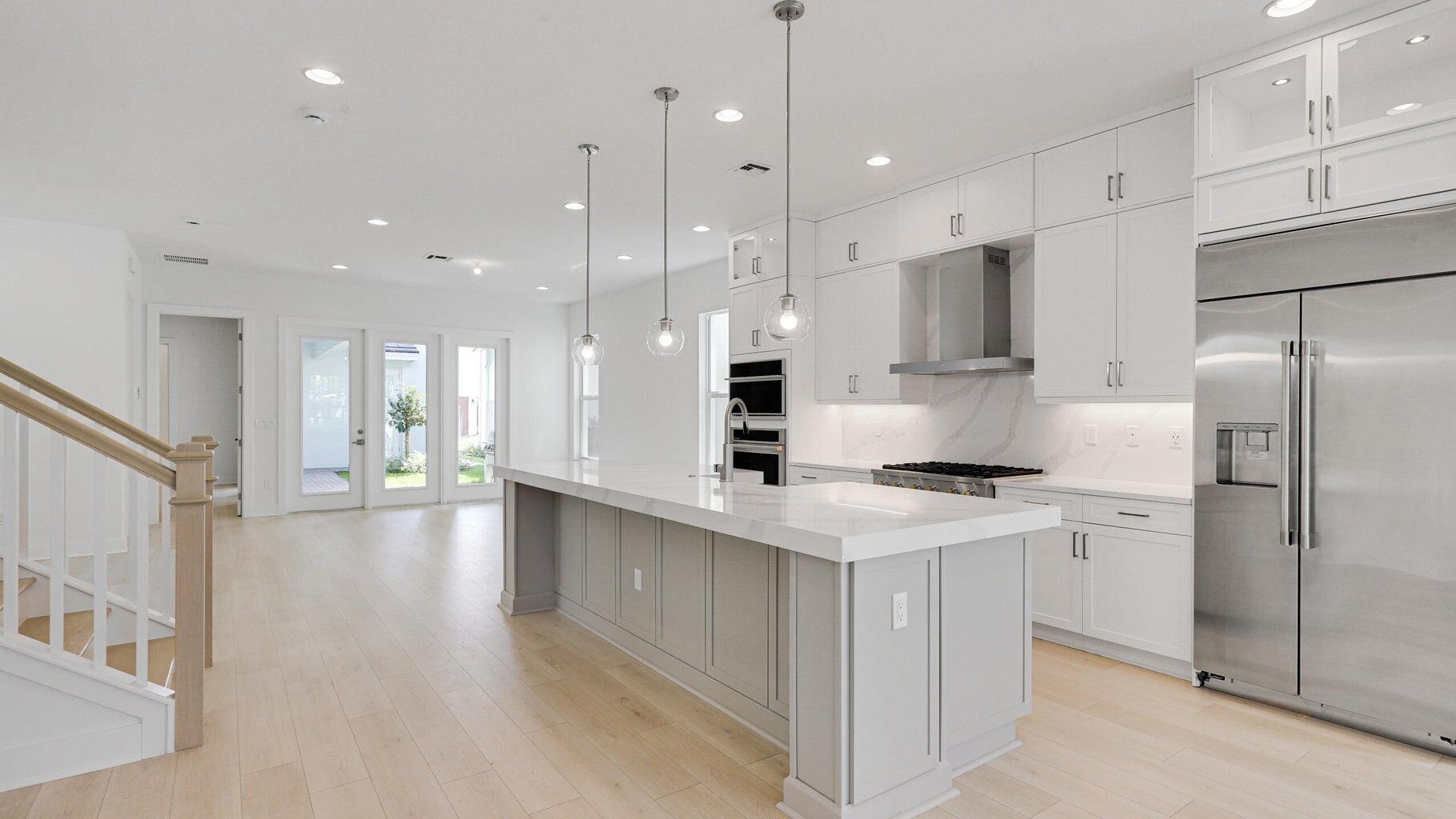 a large kitchen with stainless steel appliances kitchen island granite countertop a stove a refrigerator a oven and a white cabinets with wooden floor