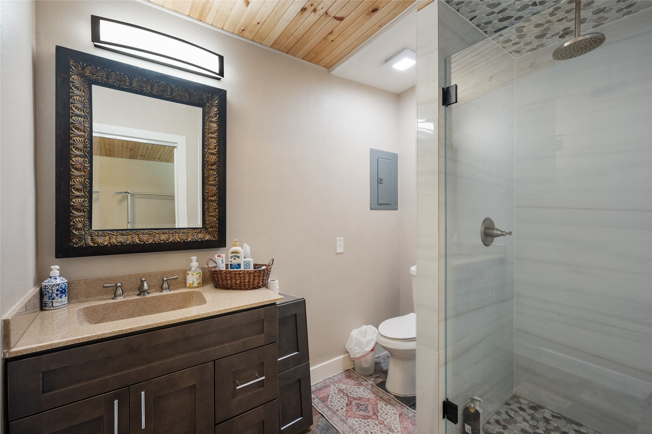 301 Oak Ridge Road Georgetown, TX 78628 - Photo 30 of 34 Contemporary bathroom featuring a dark wood vanity with a light-colored countertop, an ornate framed mirror, a glass-enclosed shower with a rain showerhead, and a natural wood-finish ceiling