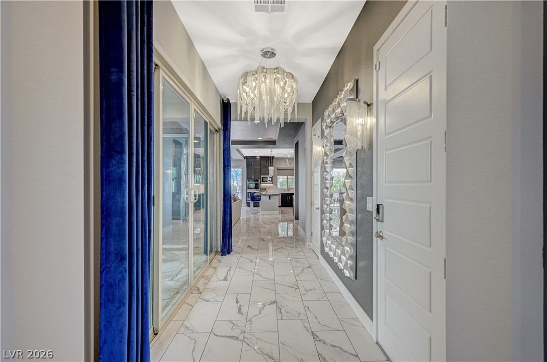 3943 Reyes Avenue Las Vegas, NV 89141 - Photo 22 of 95 Enter into a sleek hallway, guiding your gaze to a modern kitchen beyond, all illuminated by a captivating chandelier.