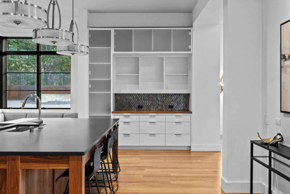 1905 Paisano Road Austin, TX 78746 - Photo 11 of 40 A streamlined kitchen island with a dark countertop anchors this luminous space, complemented by custom cabinetry and warm hardwood flooring.