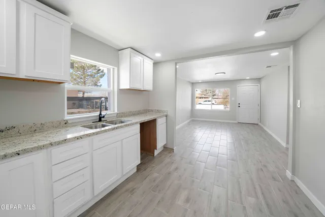 a kitchen with granite countertop a stove a sink and white cabinets with wooden floor