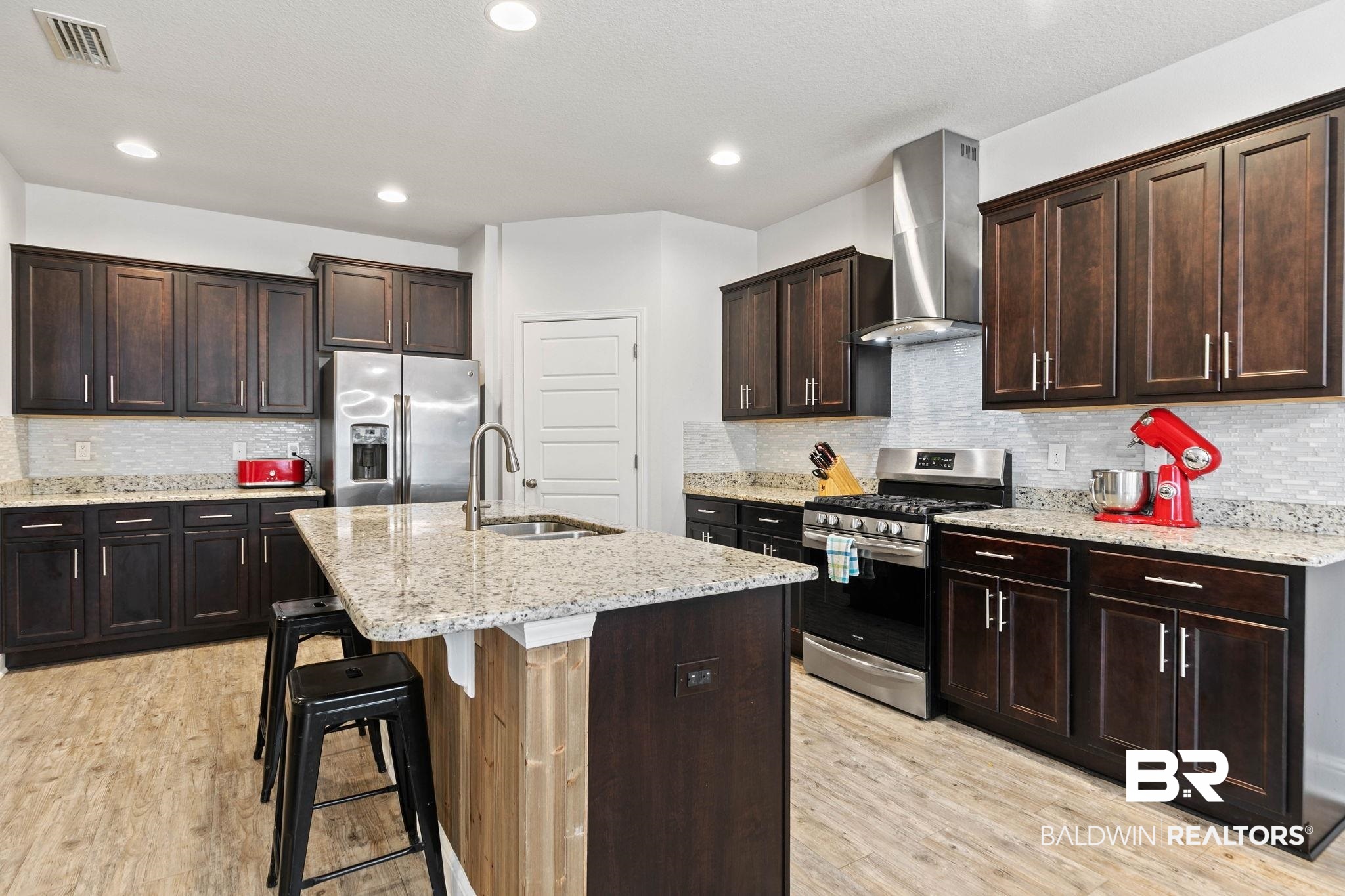 31350 Hoot Owl Road Daphne, AL 36527 - Photo 14 of 94 Kitchen featuring stainless steel appliances, dark wood finish cabinetry, light stone counters, an island with sink, and recessed lighting
