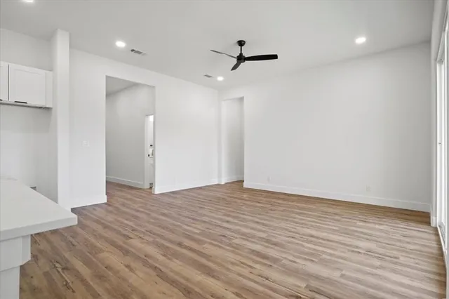a view of an empty room with wooden floor and a ceiling fan