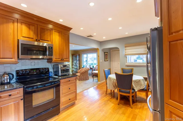 a kitchen with stainless steel appliances granite countertop a stove top oven a sink dishwasher a dining table and chairs with wooden floor