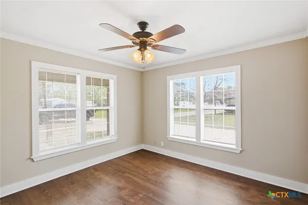 an empty room with wooden floor fan and windows