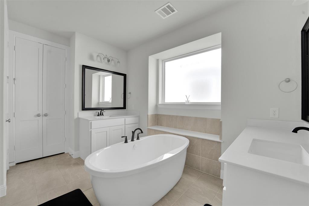 3520 Helios Lane Corinth, TX 76208 - Photo 20 of 37 Freestanding soaking tub with matte black fixtures, dual vanity sinks with white countertops, and a window above a tiled bench