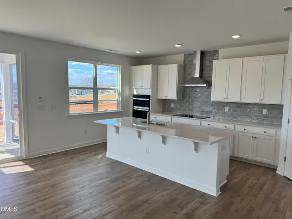 a large white kitchen with granite countertop a stove a sink a refrigerator and white cabinets with wooden floor