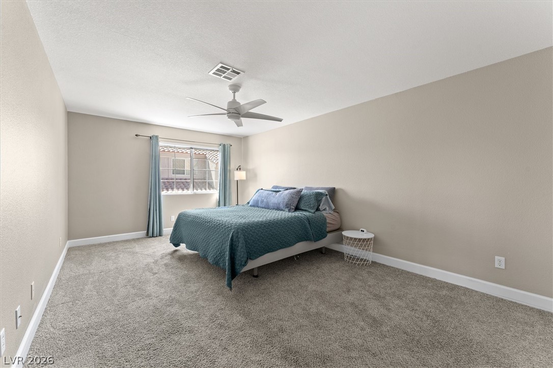 503 Rafkin Place Henderson, NV 89052 - Photo 8 of 18 A spacious bedroom features soft gray carpeting and a large window, creating a serene personal retreat.